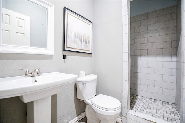 bathroom featuring sink, a tile shower, and toilet