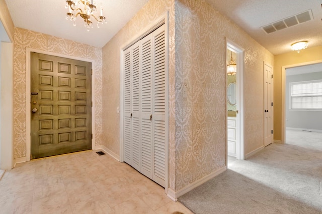 carpeted entrance foyer with a textured ceiling and a chandelier