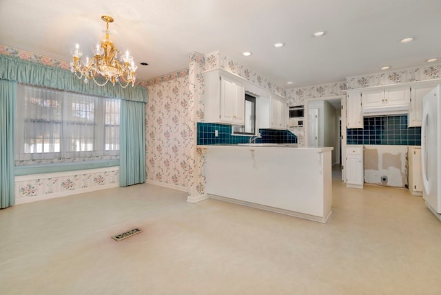 kitchen with an inviting chandelier, kitchen peninsula, hanging light fixtures, white fridge, and white cabinetry