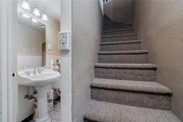 staircase featuring tile patterned floors, sink, and tile walls