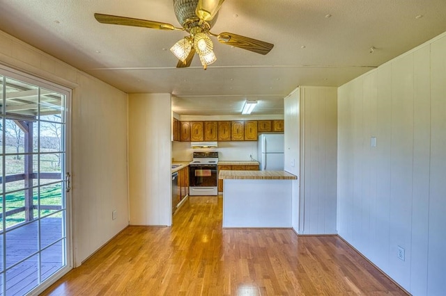 kitchen featuring ceiling fan, kitchen peninsula, light hardwood / wood-style floors, white appliances, and wooden walls