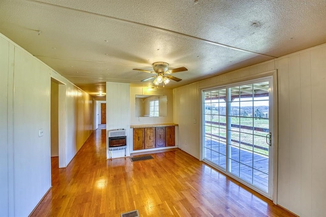 unfurnished living room featuring a textured ceiling, heating unit, light hardwood / wood-style flooring, and ceiling fan