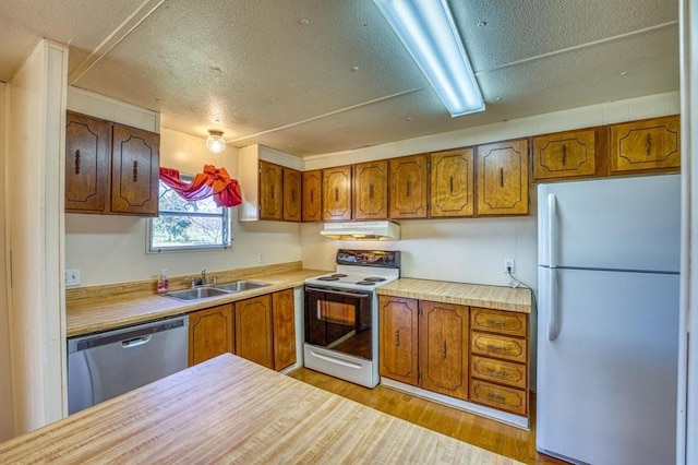 kitchen with a textured ceiling, white appliances, light hardwood / wood-style flooring, and sink