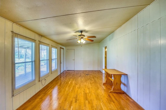 unfurnished room featuring a textured ceiling, light wood-type flooring, ceiling fan, and wood walls