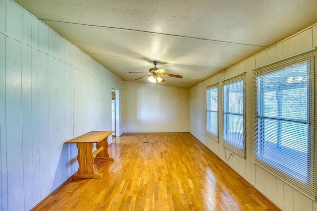 unfurnished room with a textured ceiling, light wood-type flooring, ceiling fan, and wood walls