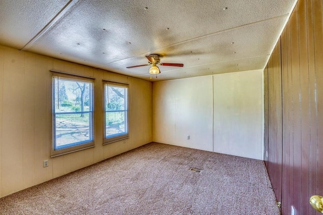 unfurnished room featuring carpet, a textured ceiling, and wooden walls