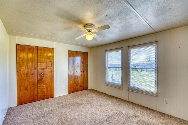 unfurnished bedroom with carpet flooring, ceiling fan, a textured ceiling, and two closets