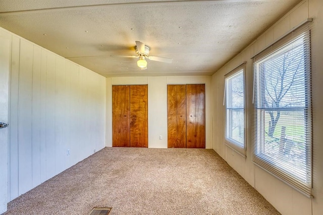 unfurnished bedroom with ceiling fan, wood walls, carpet floors, and two closets