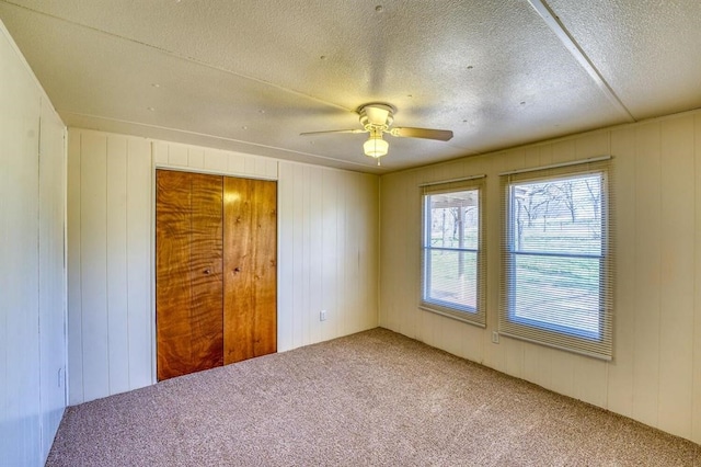 unfurnished bedroom featuring a textured ceiling, ceiling fan, carpet floors, and wood walls