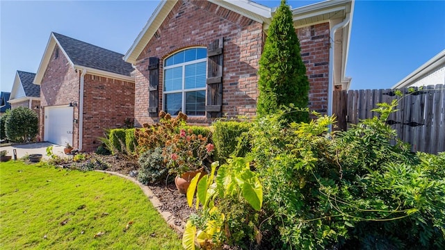 view of side of home featuring brick siding, a lawn, roof with shingles, and fence