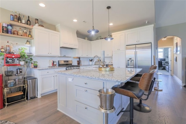 kitchen featuring custom exhaust hood, arched walkways, a sink, stainless steel appliances, and white cabinetry