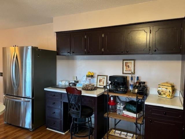 kitchen with a textured ceiling, dark hardwood / wood-style flooring, stainless steel refrigerator, and dark brown cabinetry