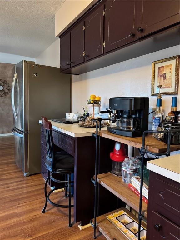 kitchen featuring a breakfast bar, light hardwood / wood-style flooring, a textured ceiling, dark brown cabinets, and stainless steel refrigerator