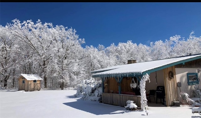 snow covered back of property featuring a shed