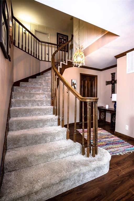 stairway with hardwood / wood-style flooring, a notable chandelier, and ornamental molding