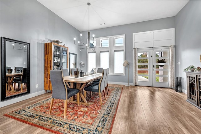 dining space featuring french doors, a towering ceiling, light hardwood / wood-style floors, and an inviting chandelier