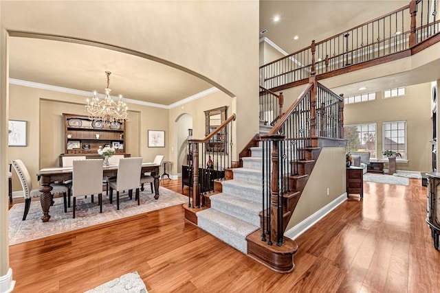 stairway with wood-type flooring, crown molding, a towering ceiling, and a chandelier