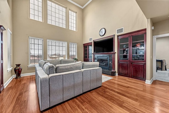 living room featuring hardwood / wood-style flooring, a towering ceiling, crown molding, and a high end fireplace