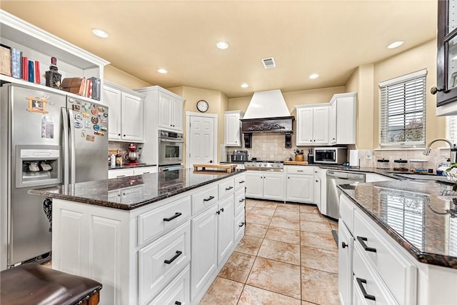 kitchen featuring white cabinets, appliances with stainless steel finishes, a kitchen island, and custom range hood