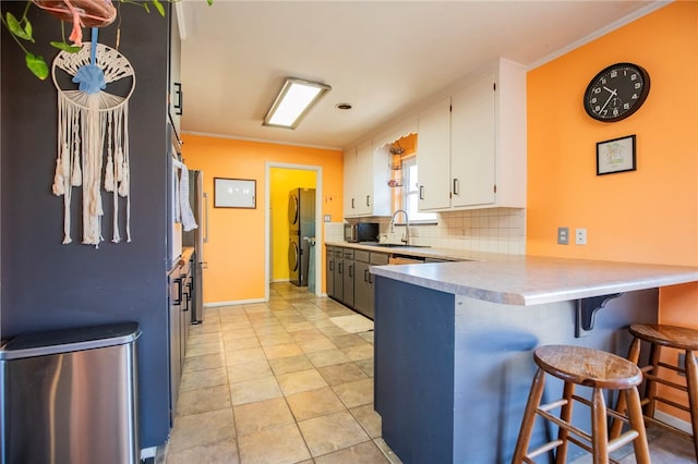 kitchen with sink, crown molding, white cabinetry, tasteful backsplash, and a kitchen bar