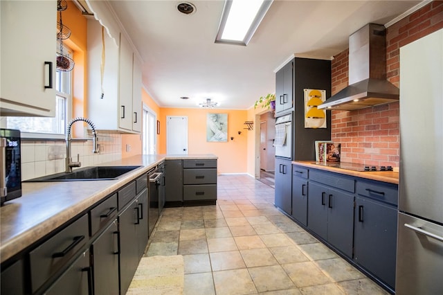 kitchen featuring sink, tasteful backsplash, appliances with stainless steel finishes, kitchen peninsula, and wall chimney range hood