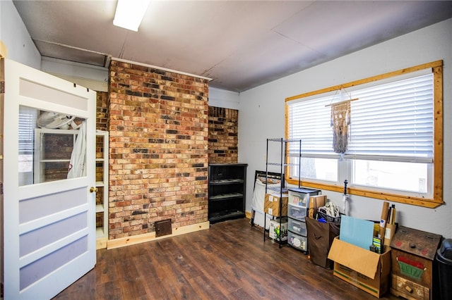 miscellaneous room featuring dark wood-type flooring and brick wall