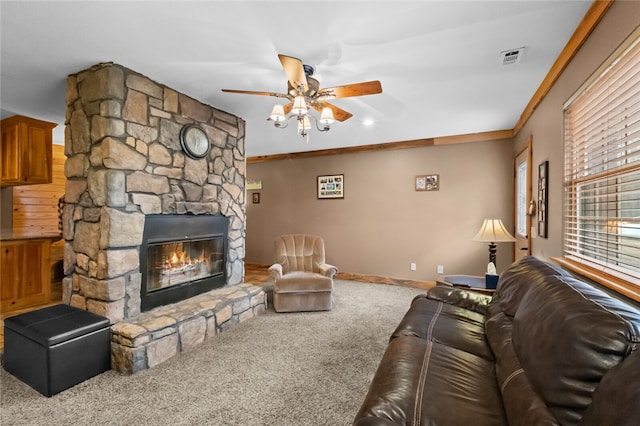 living room with carpet floors, a stone fireplace, ceiling fan, and crown molding