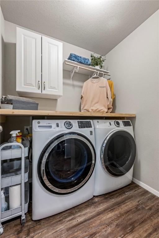 laundry area with cabinets, dark hardwood / wood-style flooring, washing machine and clothes dryer, and a textured ceiling