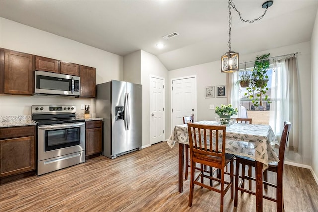 kitchen featuring lofted ceiling, appliances with stainless steel finishes, dark brown cabinetry, decorative light fixtures, and light wood-type flooring