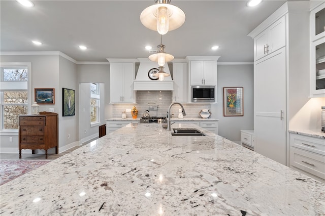 kitchen featuring sink, stainless steel microwave, white cabinetry, and hanging light fixtures