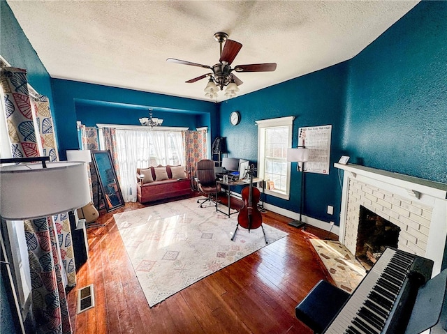 home office featuring a fireplace, ceiling fan with notable chandelier, wood-type flooring, and a textured ceiling