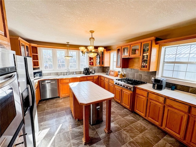 kitchen with tile counters, sink, stainless steel appliances, pendant lighting, and a chandelier