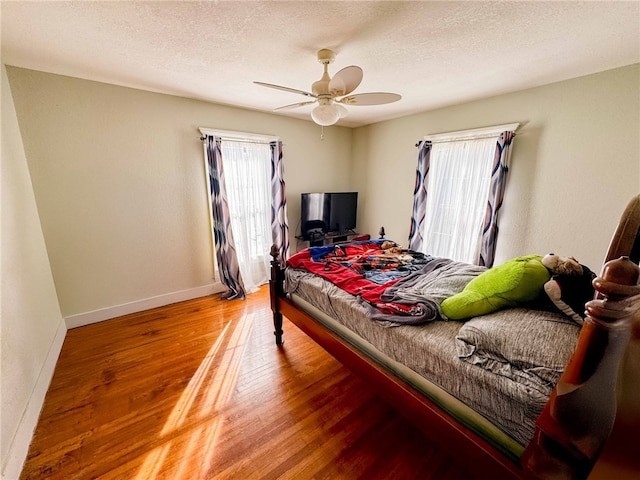 bedroom with multiple windows, ceiling fan, a textured ceiling, and hardwood / wood-style flooring