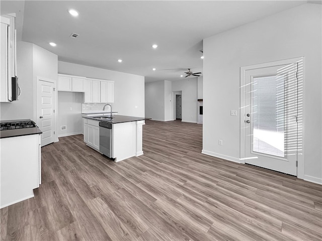 kitchen with light wood-type flooring, stainless steel dishwasher, sink, white cabinets, and an island with sink