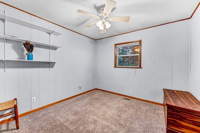 empty room featuring ceiling fan, wood walls, carpet floors, and a textured ceiling