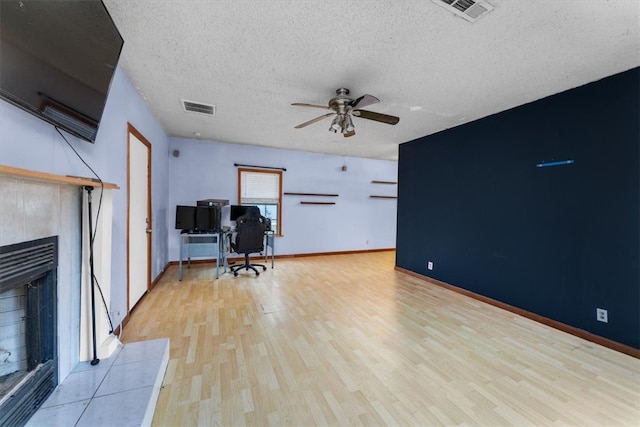 unfurnished office featuring ceiling fan, a fireplace, a textured ceiling, and light hardwood / wood-style flooring