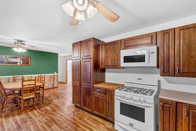 kitchen with light wood-type flooring, white appliances, and wooden walls