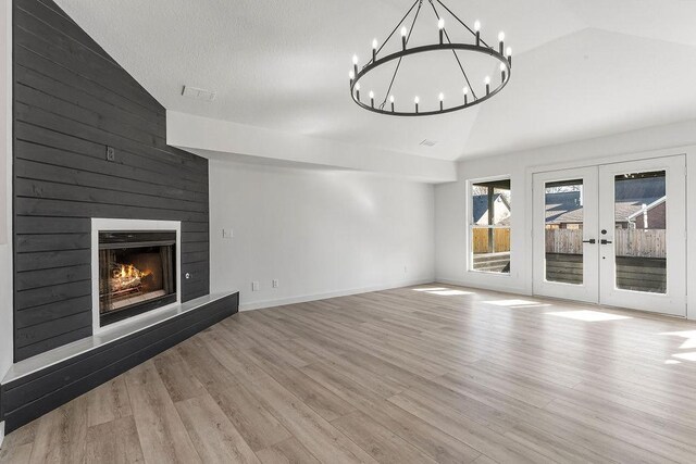 unfurnished living room featuring a fireplace, french doors, light hardwood / wood-style floors, and vaulted ceiling