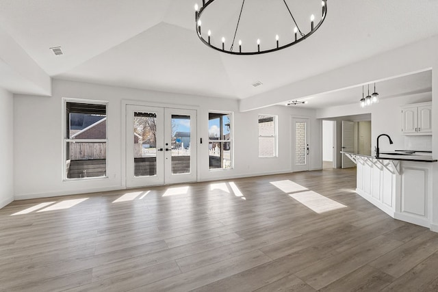 unfurnished living room with a chandelier, french doors, light wood-type flooring, and high vaulted ceiling