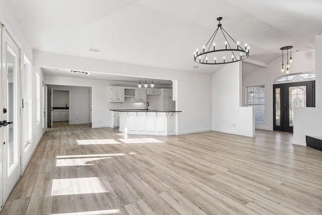 unfurnished living room with an inviting chandelier, french doors, sink, light hardwood / wood-style flooring, and vaulted ceiling