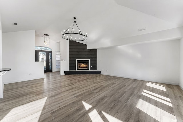 unfurnished living room with hardwood / wood-style flooring, a notable chandelier, a large fireplace, and vaulted ceiling