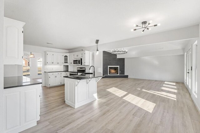 kitchen featuring light hardwood / wood-style flooring, a chandelier, a fireplace, white cabinets, and appliances with stainless steel finishes