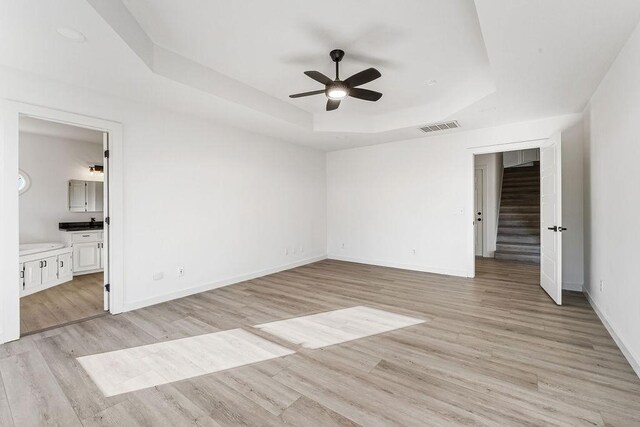 unfurnished bedroom featuring ceiling fan, light hardwood / wood-style floors, a raised ceiling, and connected bathroom