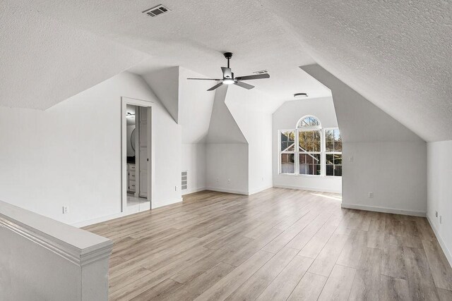 additional living space featuring ceiling fan, vaulted ceiling, a textured ceiling, and light hardwood / wood-style flooring