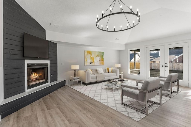 living room with lofted ceiling, a large fireplace, light hardwood / wood-style flooring, and french doors