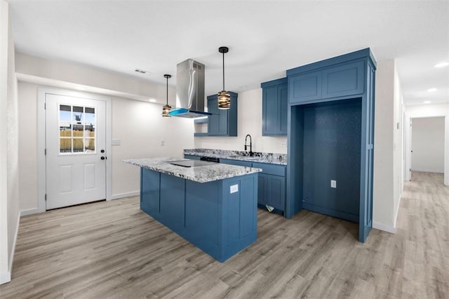 kitchen with pendant lighting, sink, light stone counters, island range hood, and light hardwood / wood-style floors