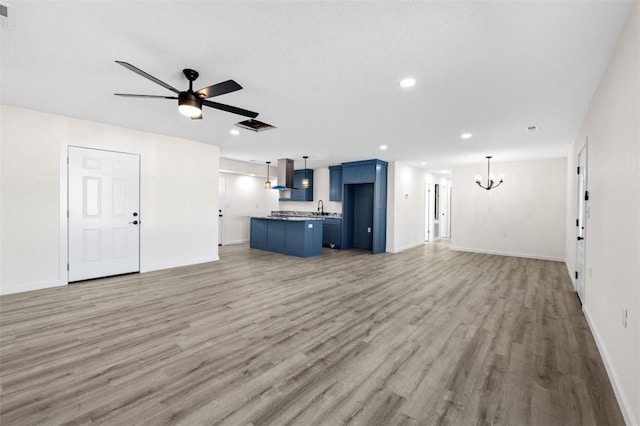 unfurnished living room with hardwood / wood-style flooring, sink, and ceiling fan with notable chandelier