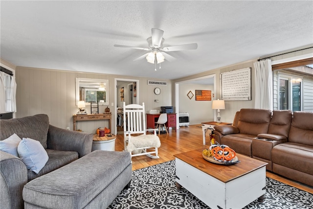 living room with wooden walls, light hardwood / wood-style flooring, ceiling fan, a textured ceiling, and heating unit