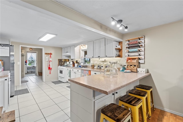 kitchen with a kitchen breakfast bar, white range, kitchen peninsula, sink, and white cabinetry