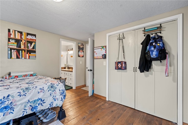 bedroom with connected bathroom, sink, dark hardwood / wood-style floors, and a textured ceiling